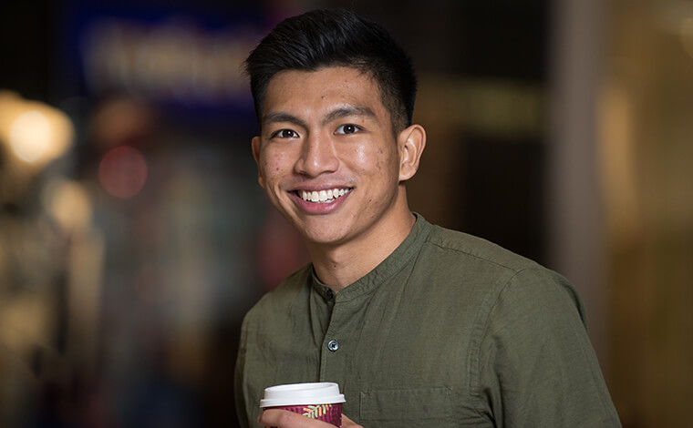 A student holding a coffee and smiling