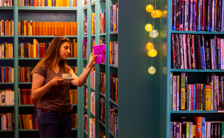 A student browsing a colourful book shelf with a cup of coffee