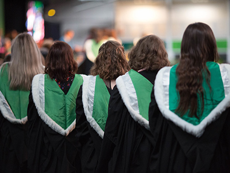 Five students in part-green robes waiting at graduation ceremony