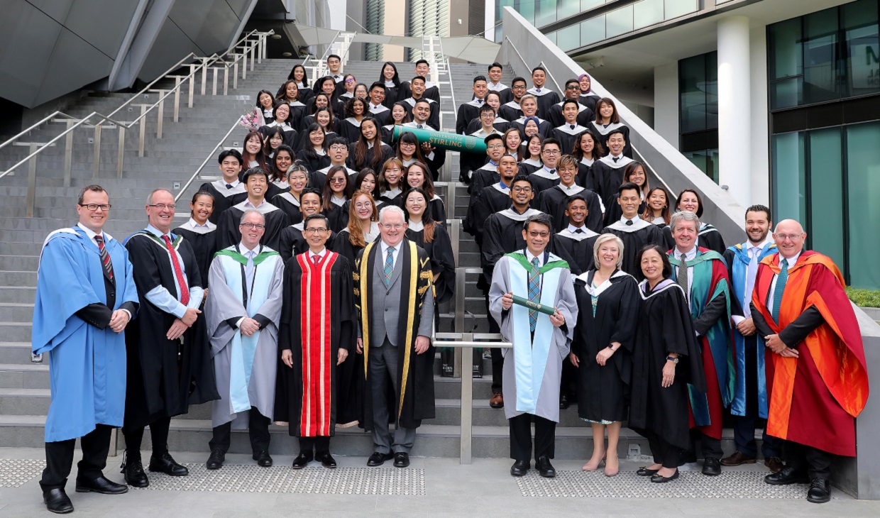 Senior staff and students in graduation robes standing on stairs