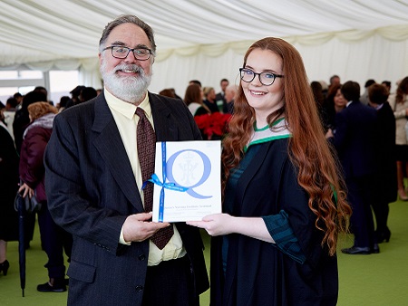 man with beard presenting award to woman in graduation gown
