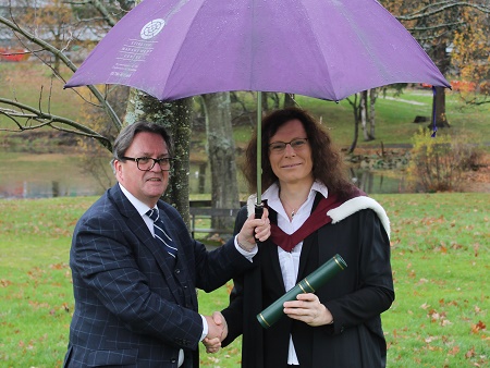 Man in suit and woman in graduation robes under umbrella