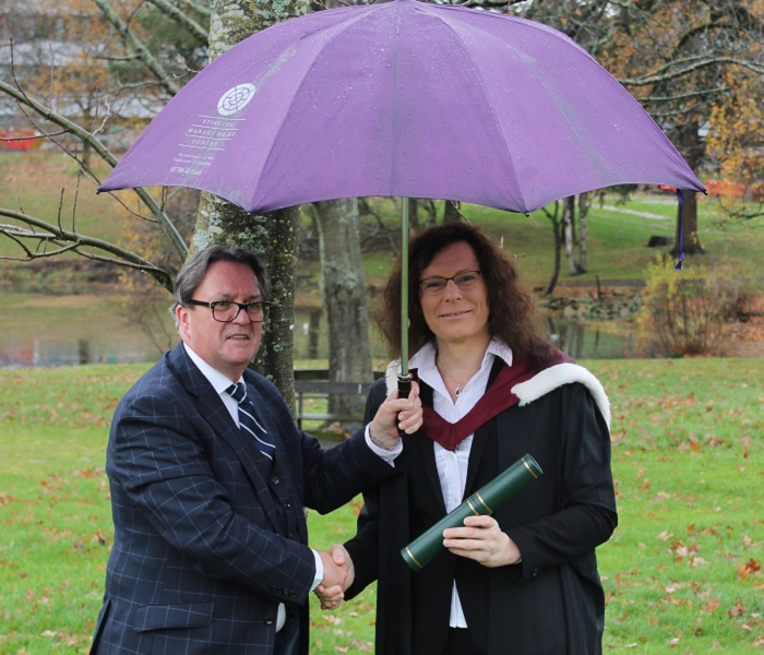 man in suit and woman in graduation robes under an umbrella