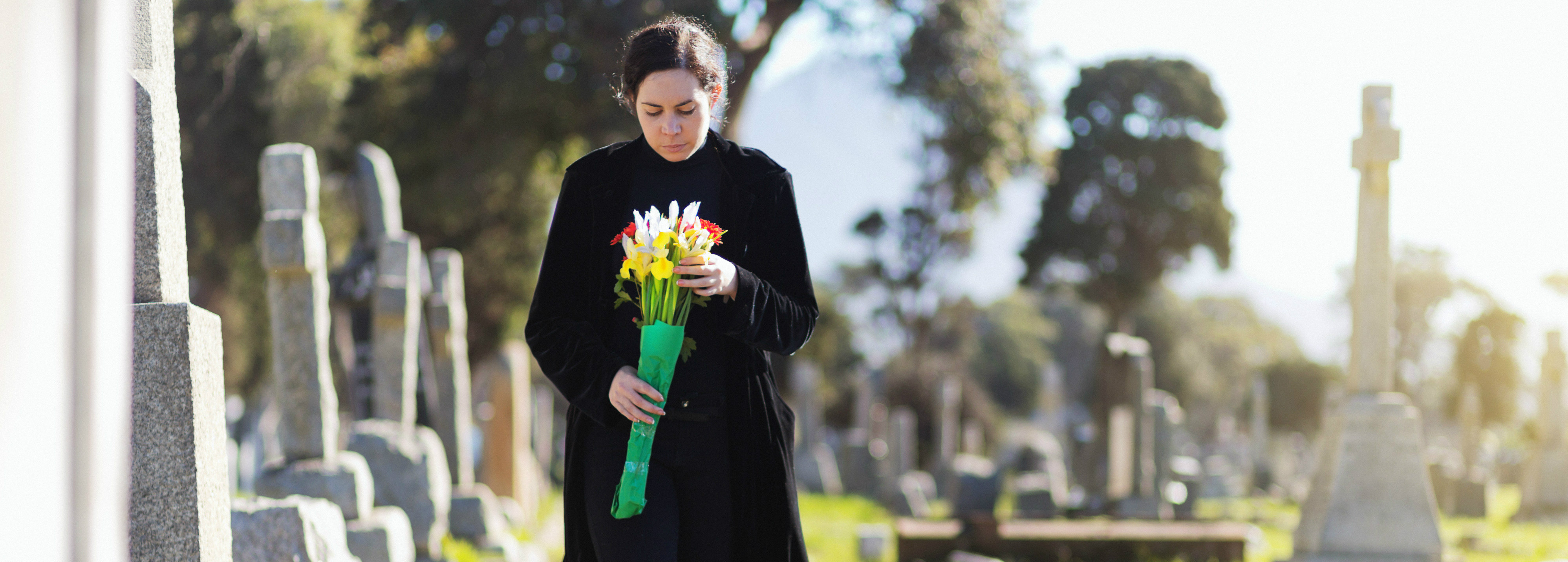 Woman wlaking through graveyard holding flowers