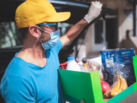 Delivery guy with protective mask and gloves delivering groceries during lockdown and pandemic.