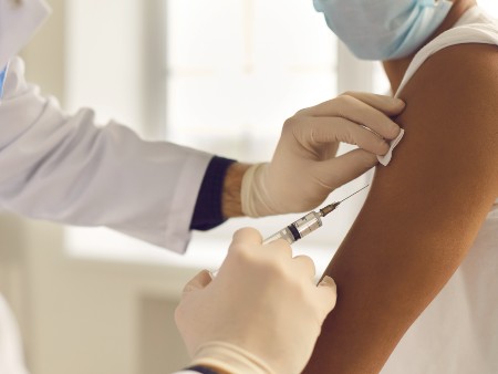 Doctor in medical gloves giving vaccine jab to patient. Close-up of hands holding syringe and cleaning skin on upper arm before antiviral injection