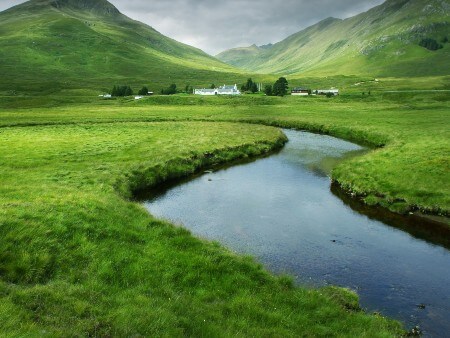 Photograph of a river surrounding by green grass and mountains