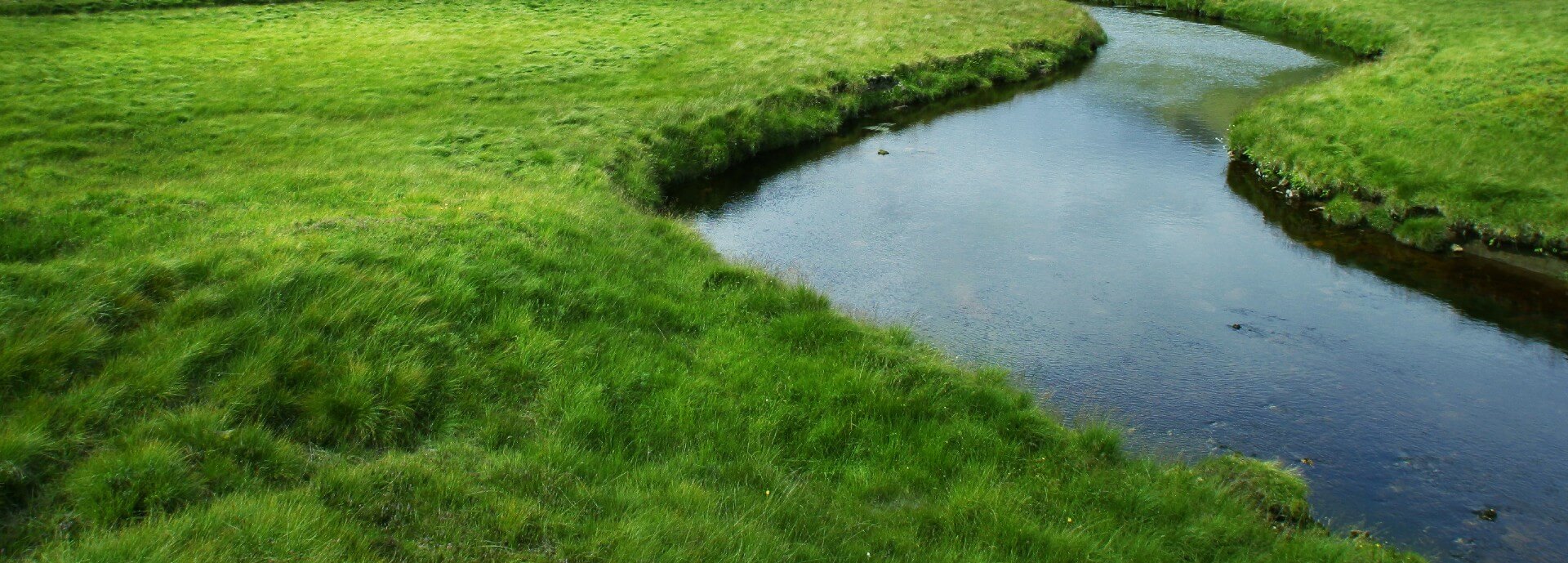 Photograph of a river surrounded by green grass and mountains