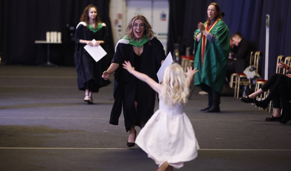 Little girl runs towards a graduating relative/friend