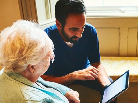 Healthcare worker with senior woman using digital tablet at care home