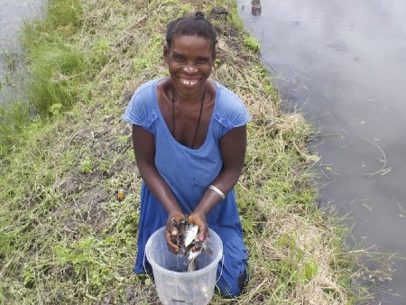 A woman photographed on the banks of a river with a bucket of fish
